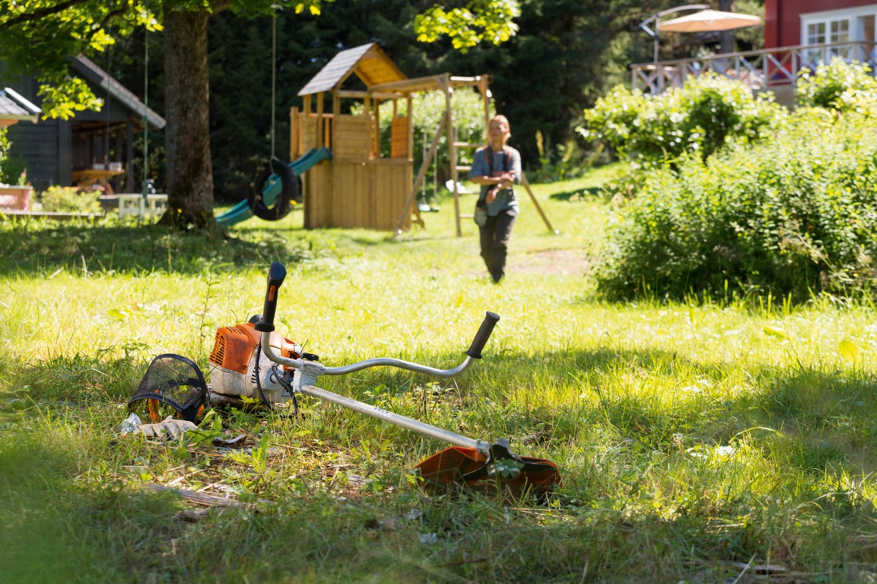 Kosa mechaniczna STIHL FS 240 leży w trawie, w tle mężczyzna przygotowuje się do konserwacji