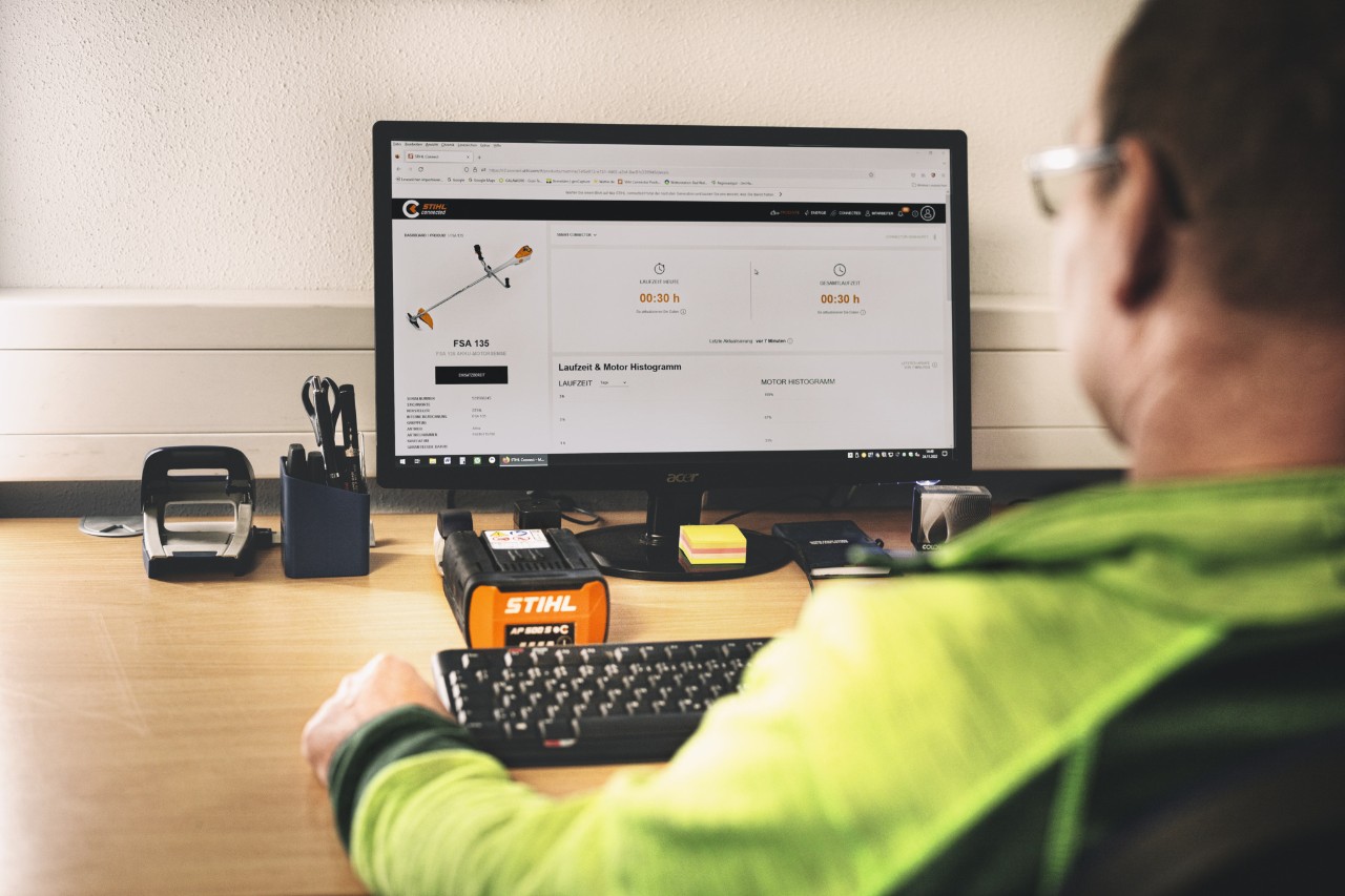 Mężczyzna siedzi w biurze przed komputerem z otworzonym portalem STIHL connected